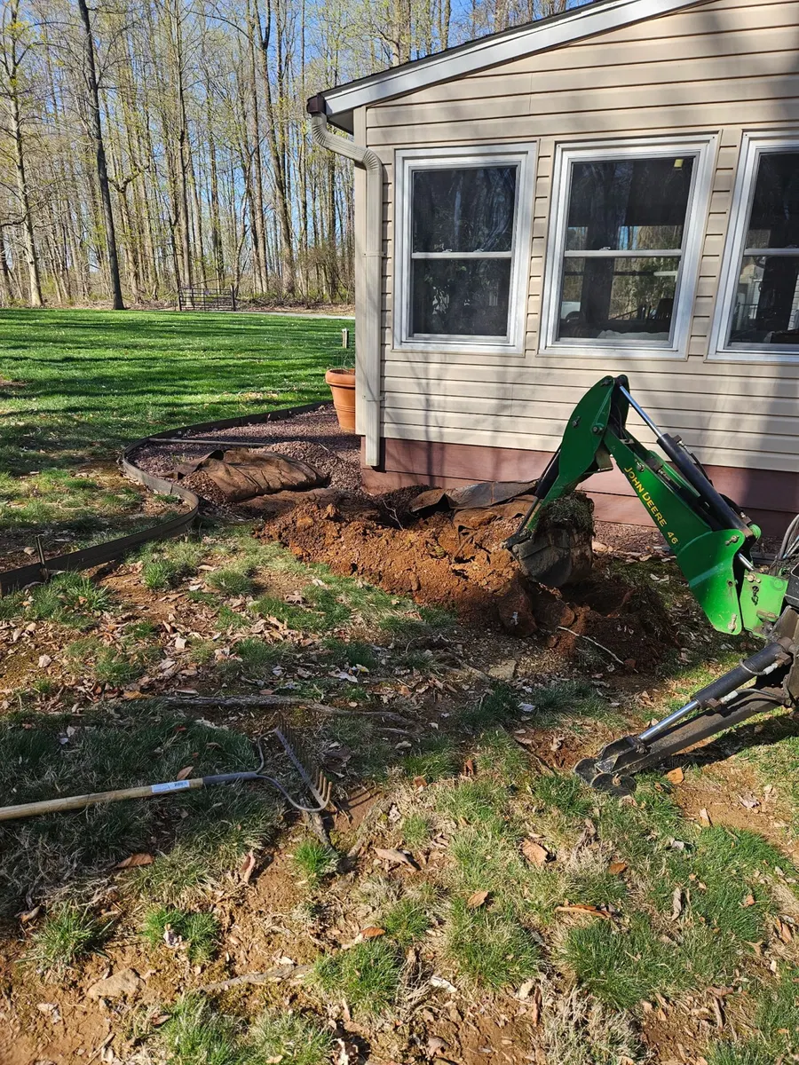 Small backhoe digging beside a home for drainage work