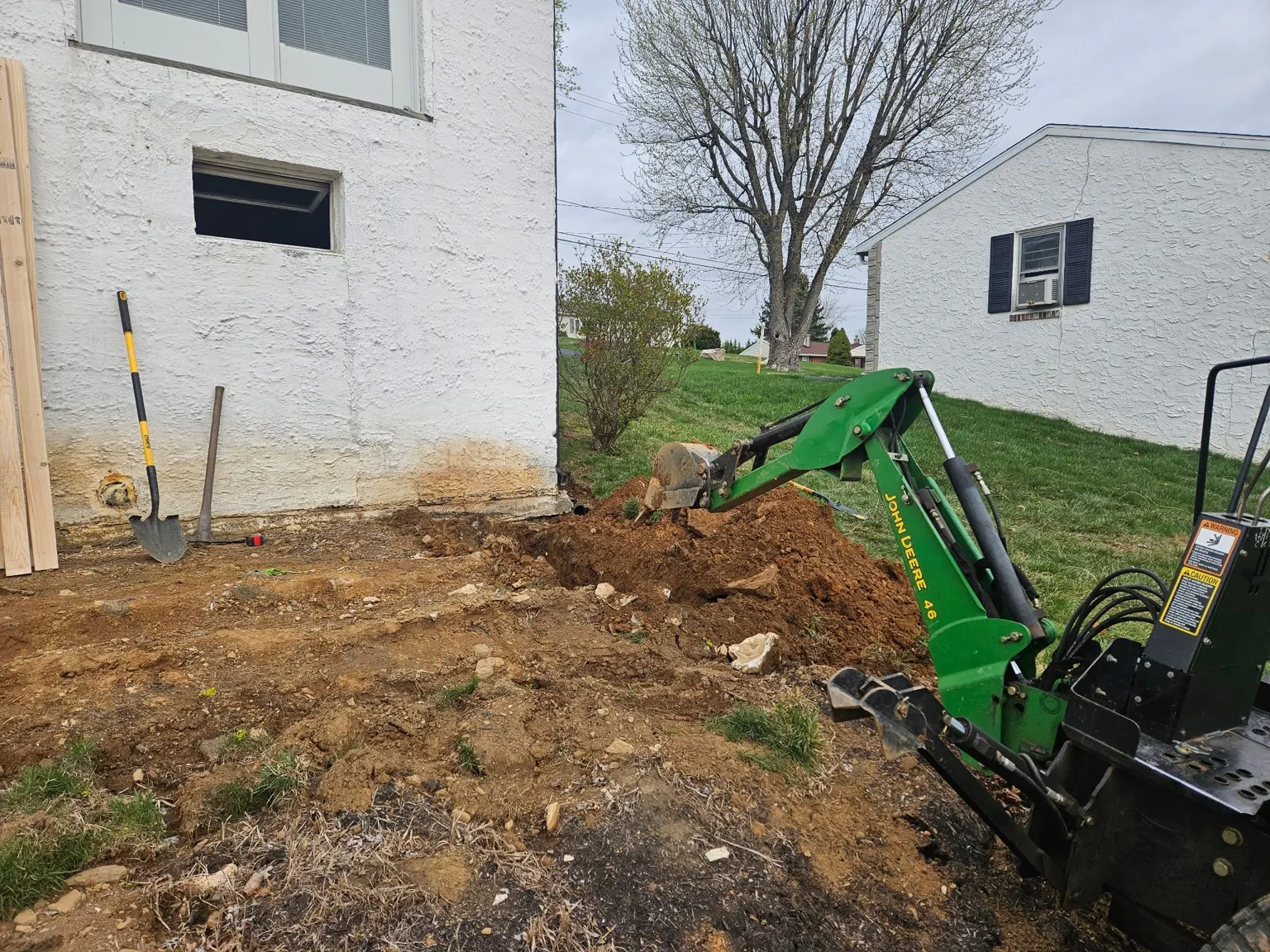 Compact backhoe excavating soil beside a house foundation