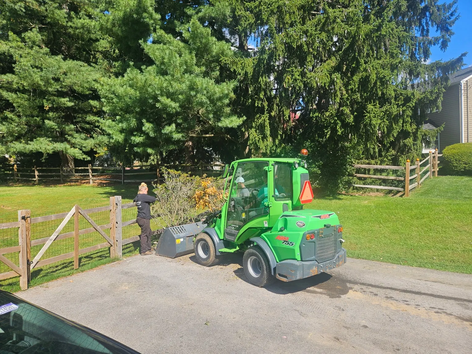 Green compact loader beside a driveway during property cleanup