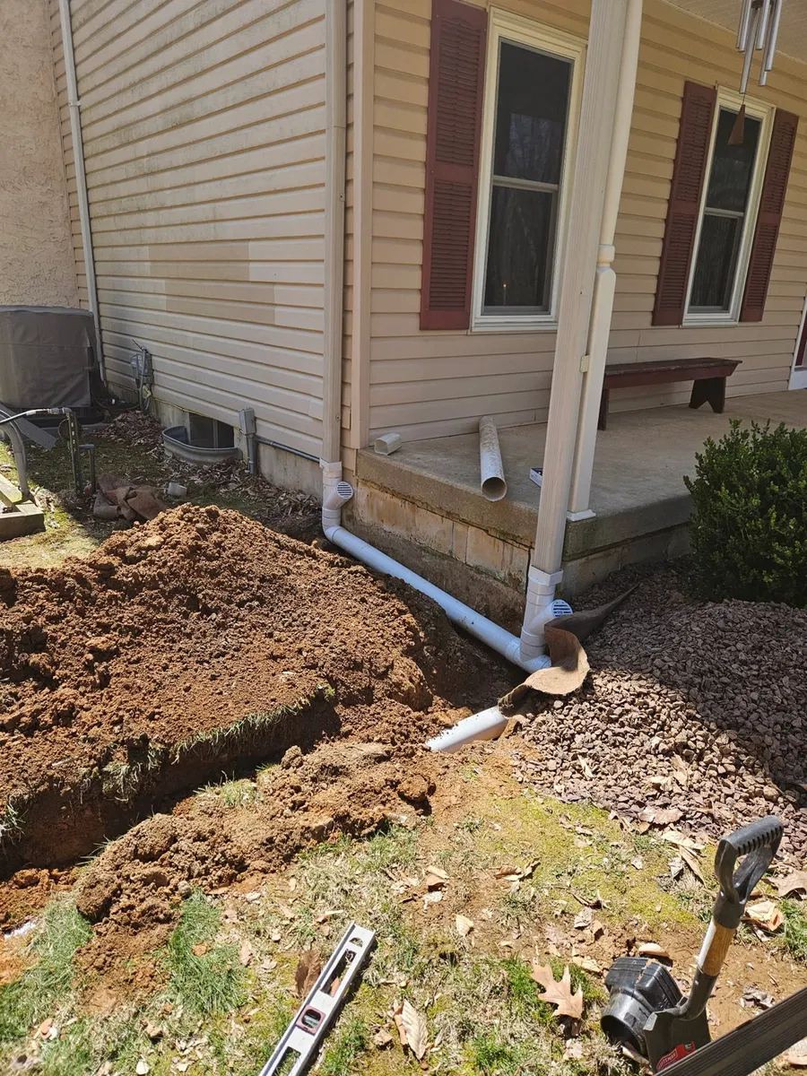 Downspout connected to drainage pipe beside a house foundation