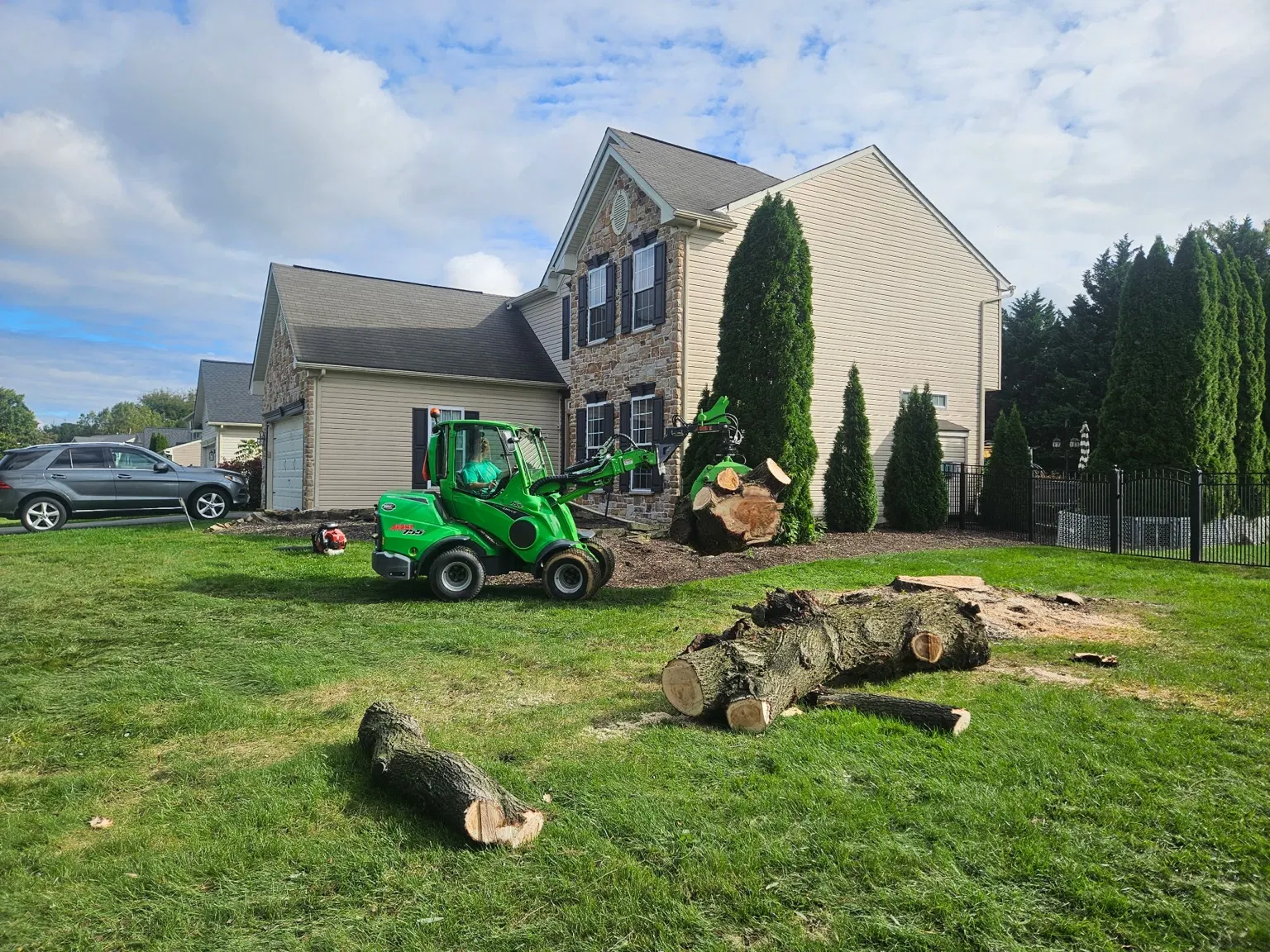 Compact loader carrying a cut log across a lawn near a home