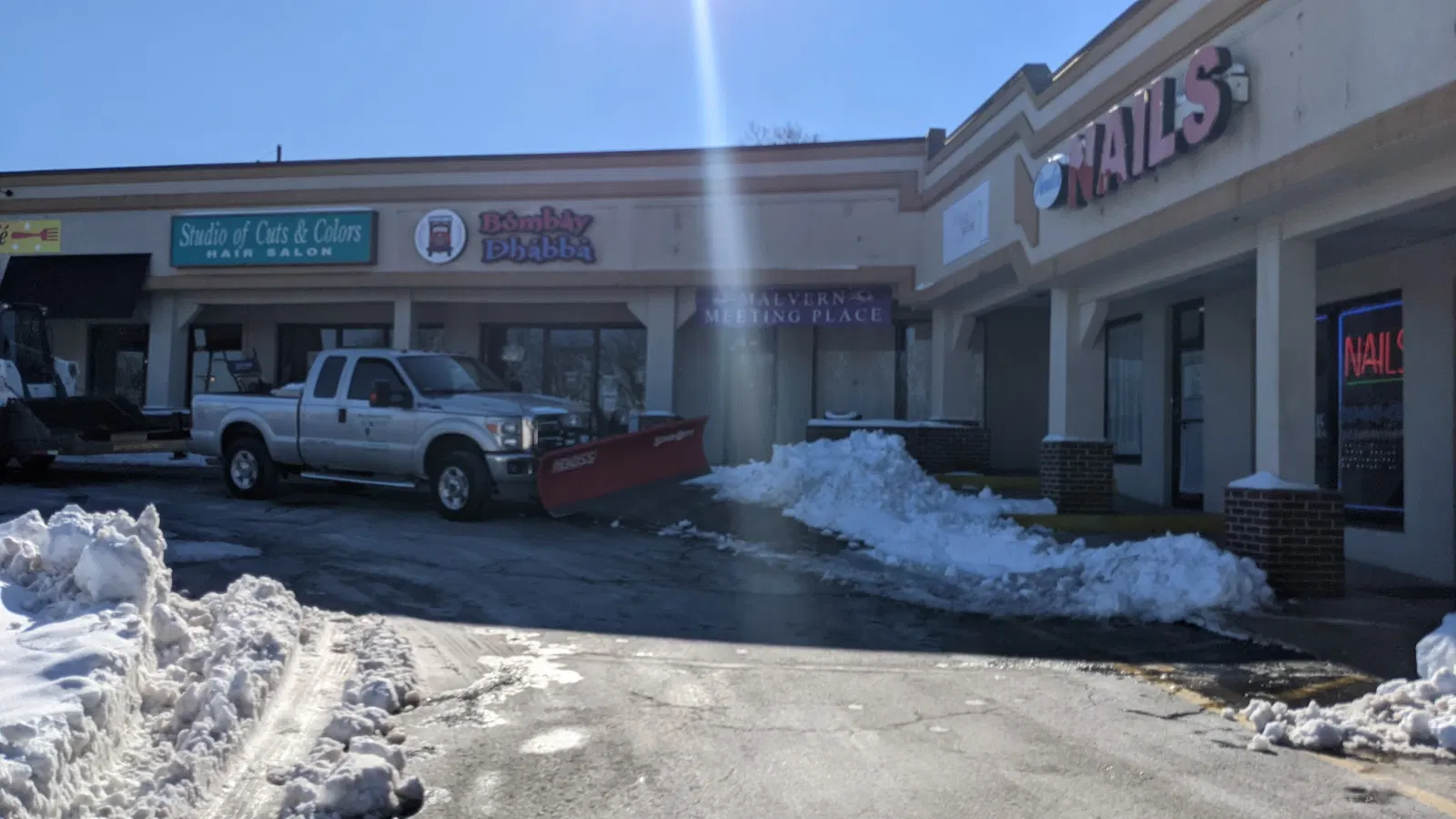 Pickup truck with a snowplow outside shopping center storefronts