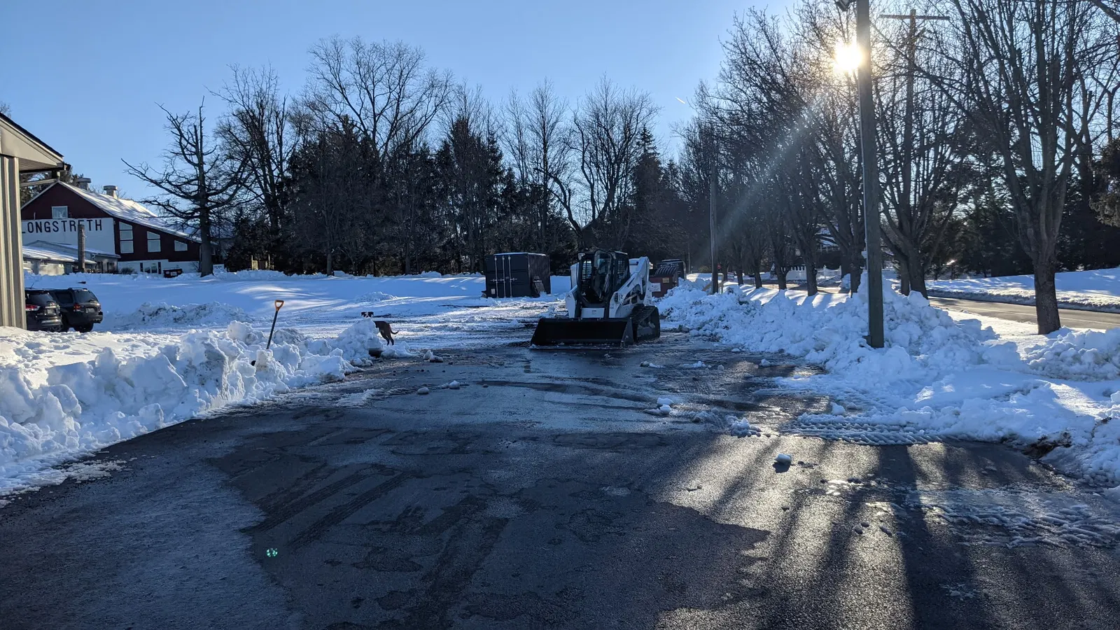 Compact loader clearing a paved area bordered by snowbanks