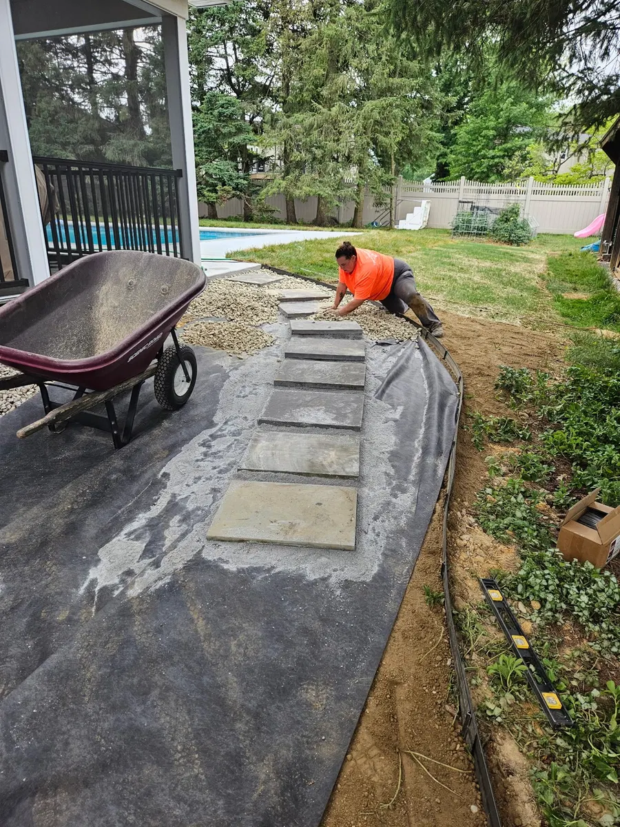 Worker installing a stepping stone path over landscape fabric beside a patio