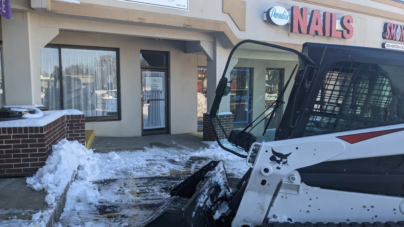 Compact loader beside a storefront during snow clearing