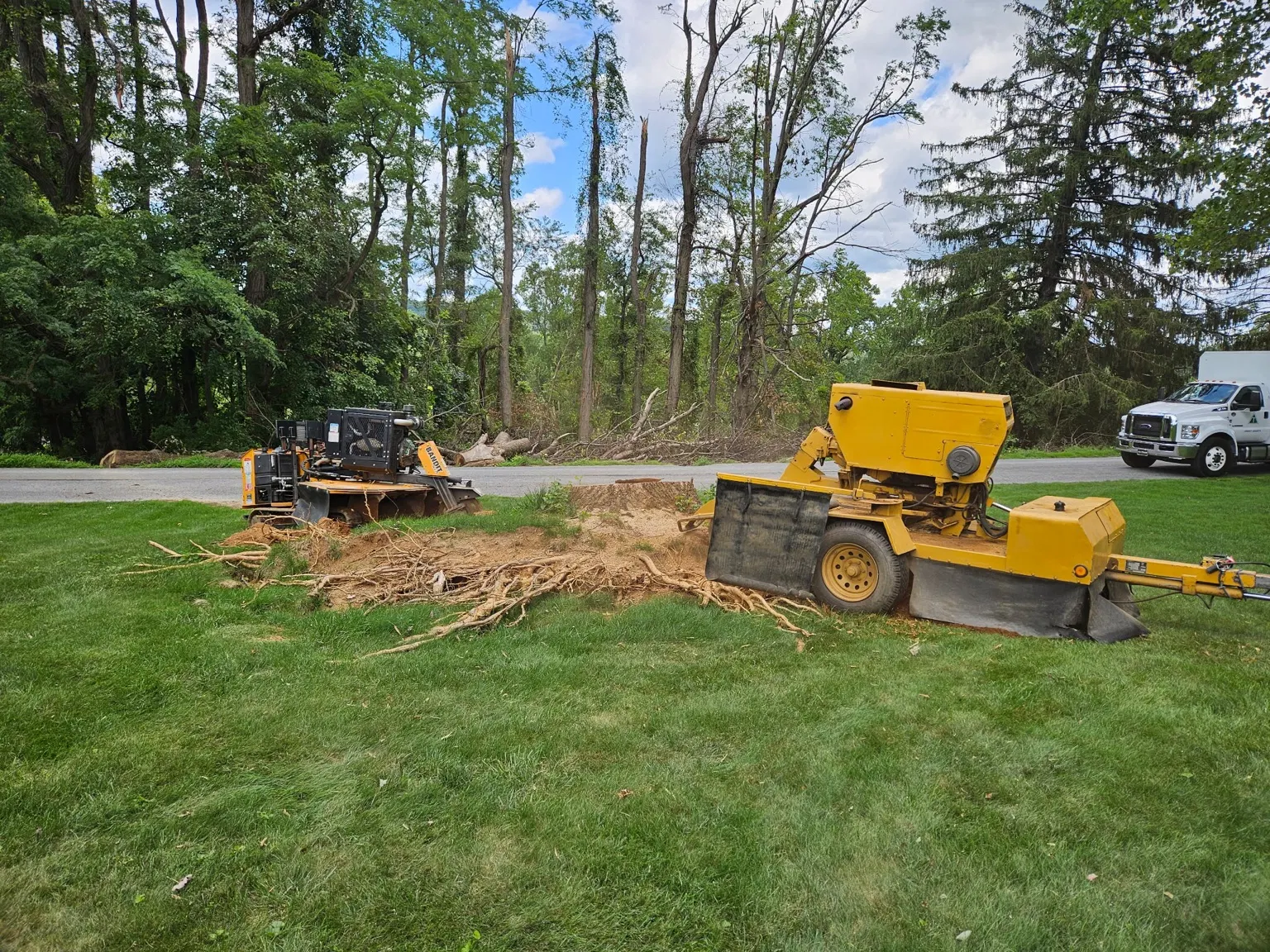 Stump grinder beside wood chips and cut branches near a road