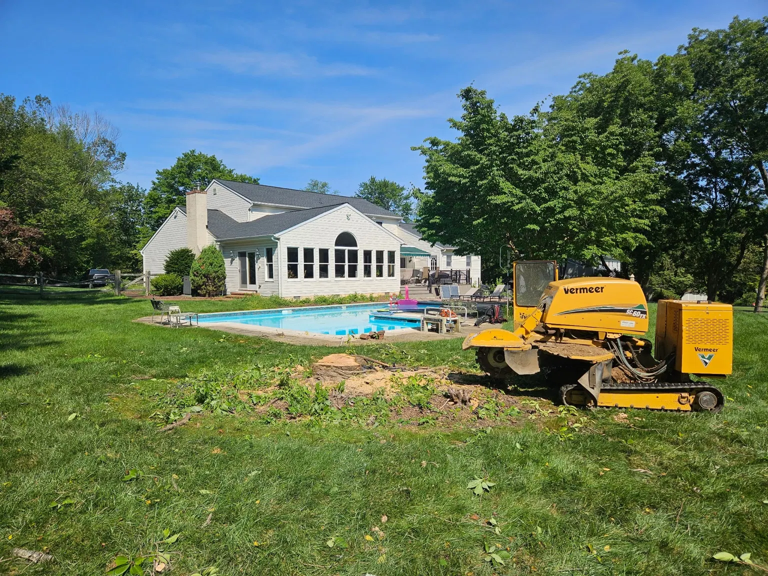 Stump grinding equipment on a lawn beside a residential swimming pool