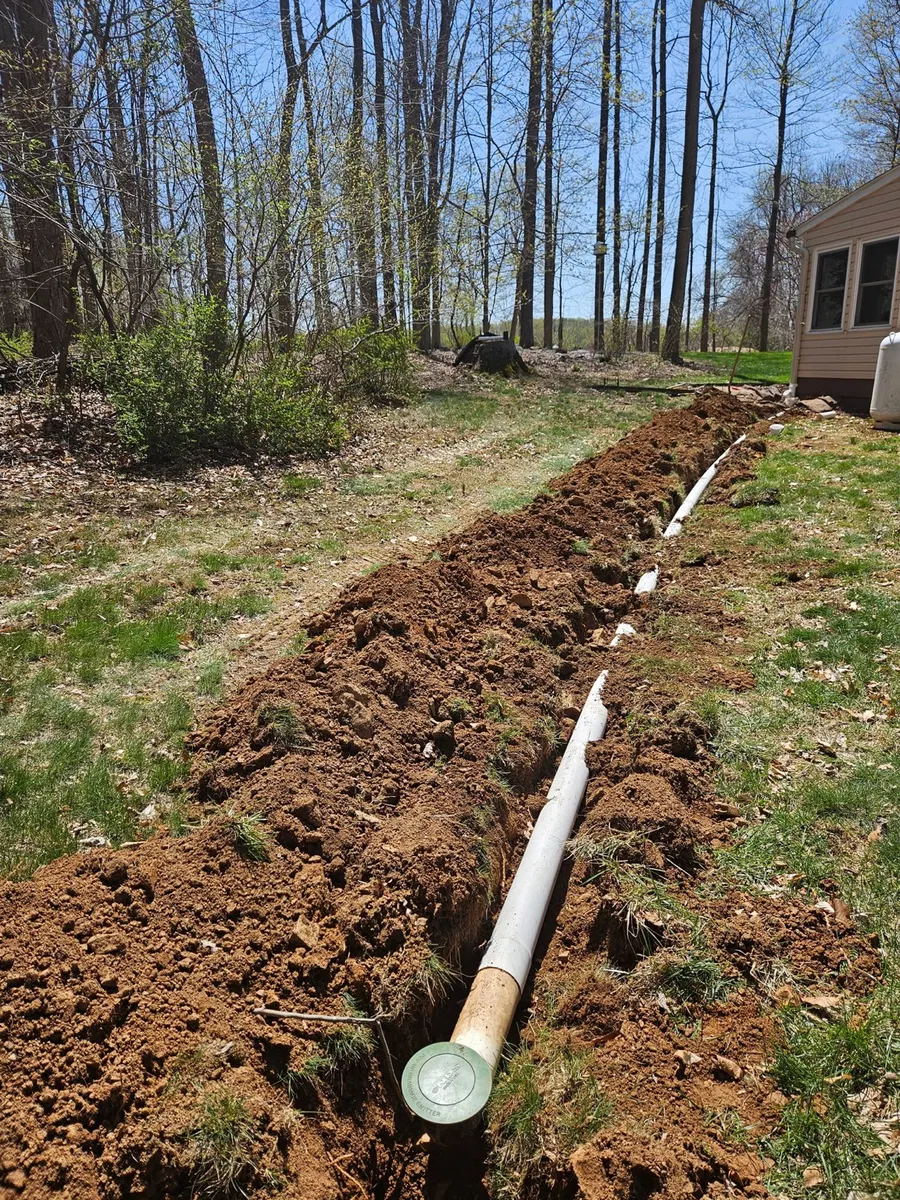 White drainage pipe in an open trench leading away from a house